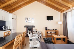 A cozy living room with a fireplace, wooden furniture, a flat-screen TV, and a dining area with a black countertop and chairs. - Aldeia das Adegas (Sao Roque do Pico)