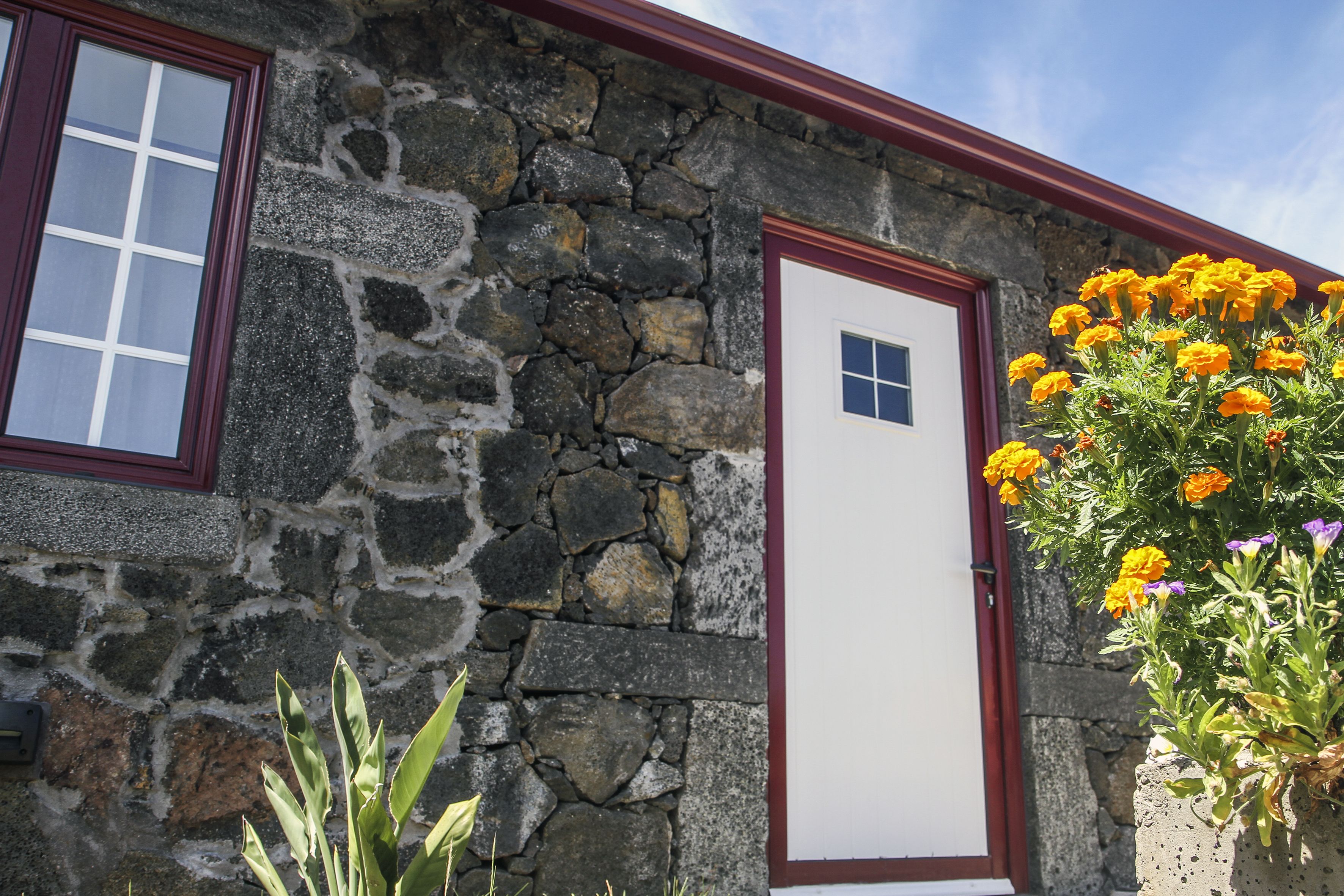 A stone building with a white door and a window with a red frame.
