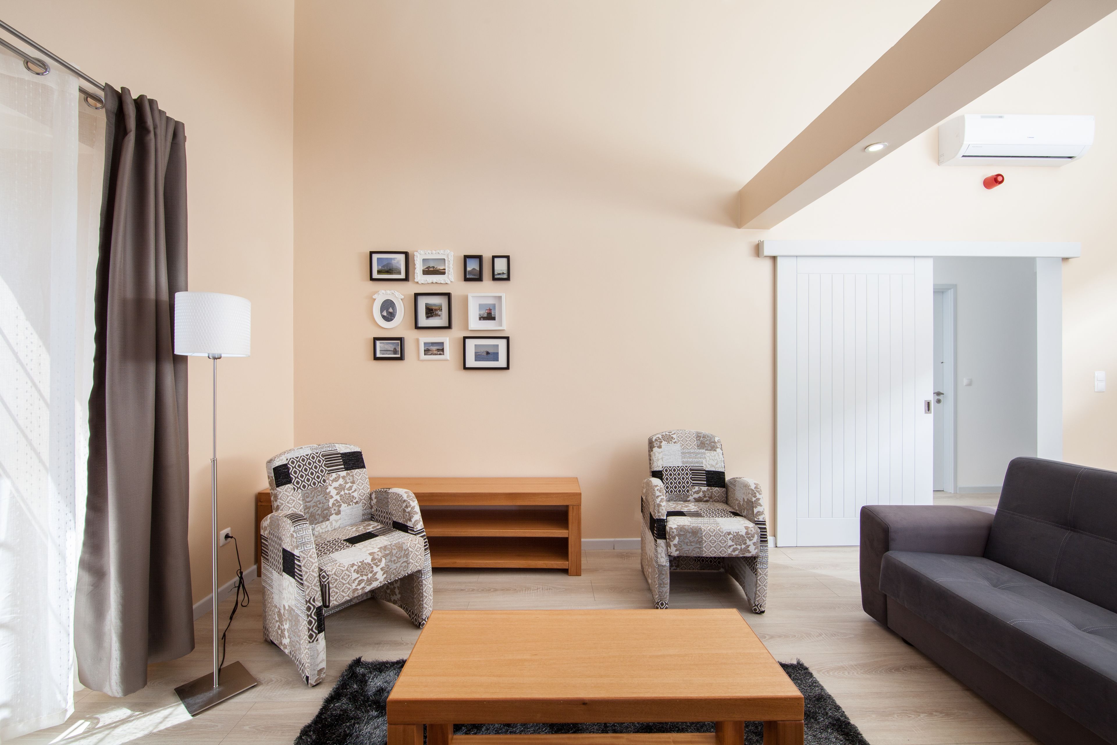 A living room with a sofa, two patterned armchairs, a wooden coffee table, a floor lamp, and a wall with framed pictures.