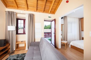 A hotel room with a wooden ceiling, a sofa, a bed, a desk with a lamp, and a view of the outside. - Aldeia das Adegas (Sao Roque do Pico)