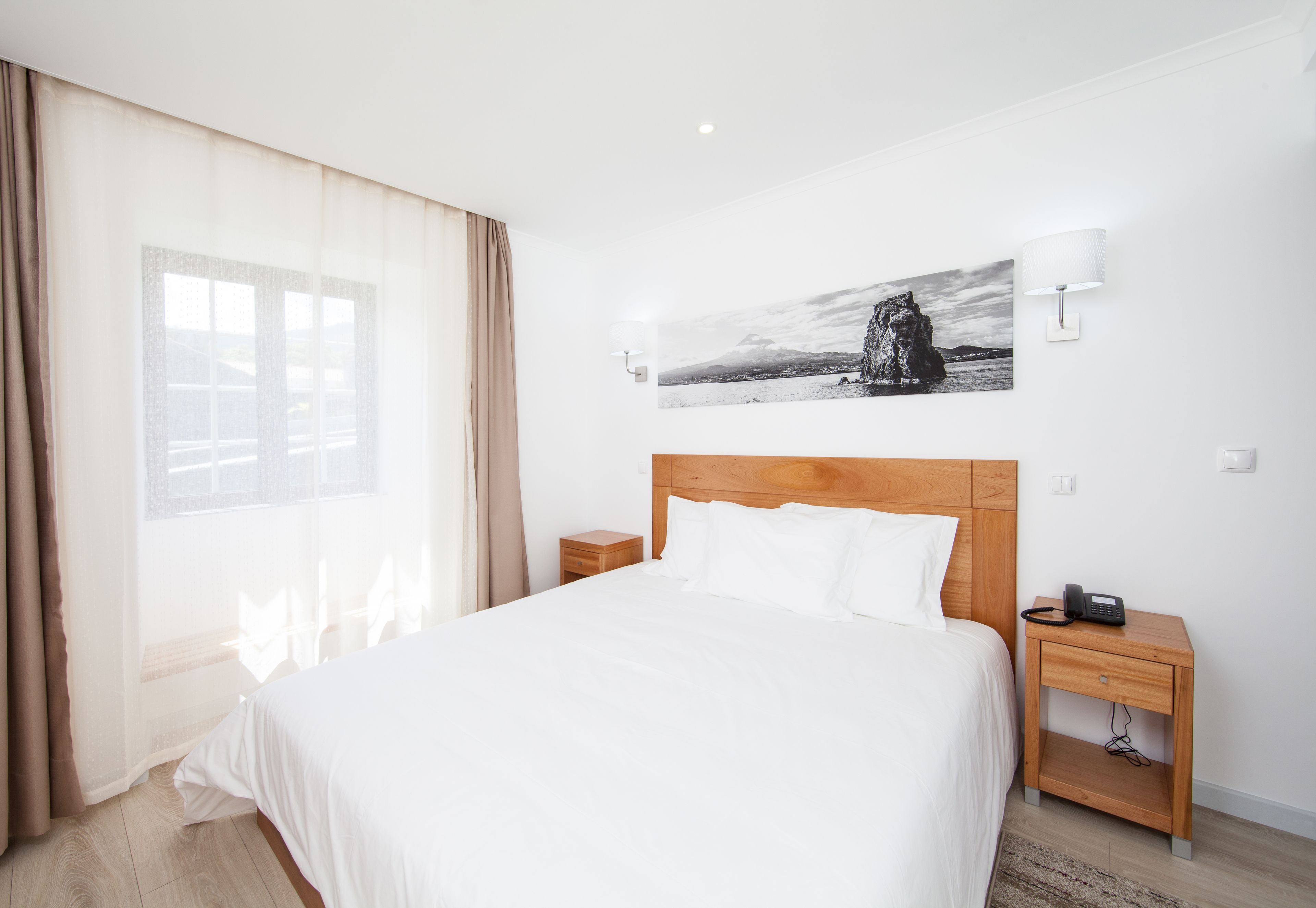 Camera d'albergo con un letto grande, un comodino con il telefono, una lampada a parete e una finestra con tende.