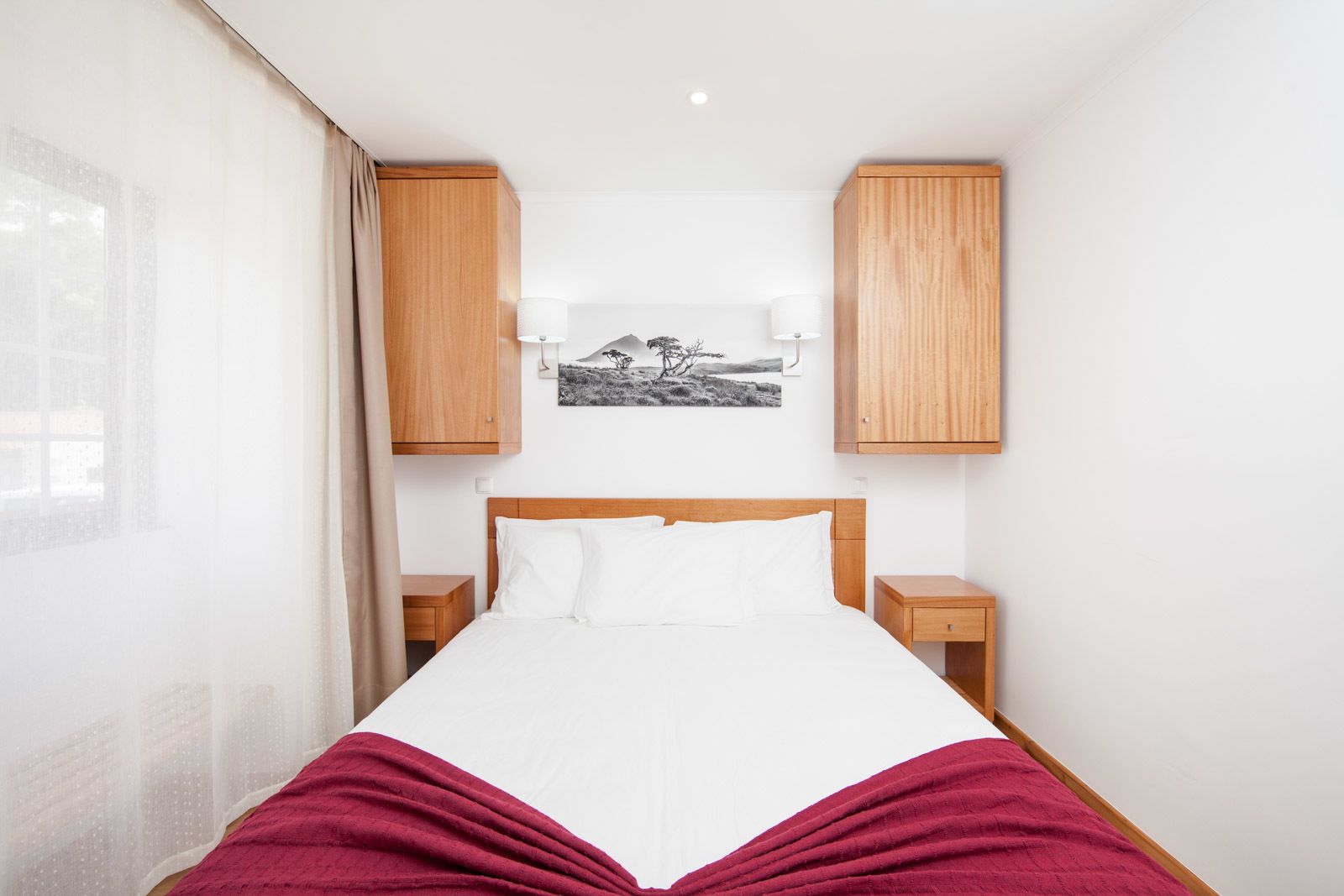 A bedroom with a bed, wooden cabinets, a nightstand, and a wall-mounted lamp.