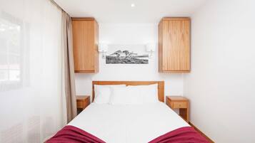 A bedroom with a bed, wooden cabinets, a nightstand, and a wall-mounted lamp.