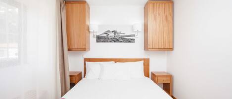 A bedroom with a bed, wooden cabinets, a nightstand, and a wall-mounted lamp.