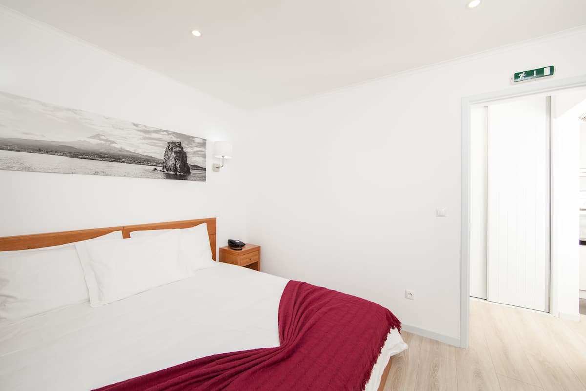 Un dormitorio con cama, mesita de noche, luz empotrada, puerta y vistas al exterior.
