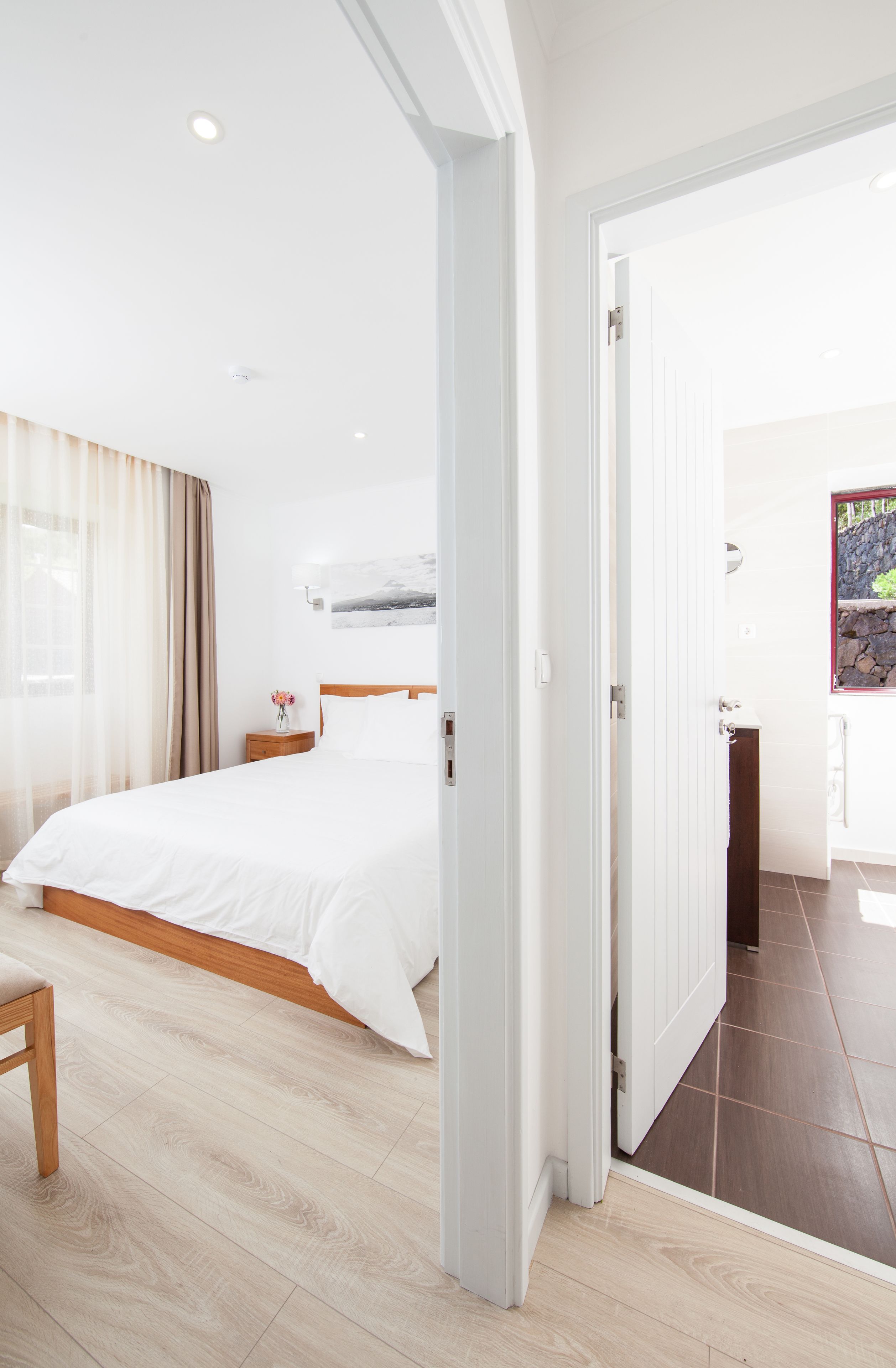 A modern hotel room with a large bed, wooden floor, and a view of the outside.