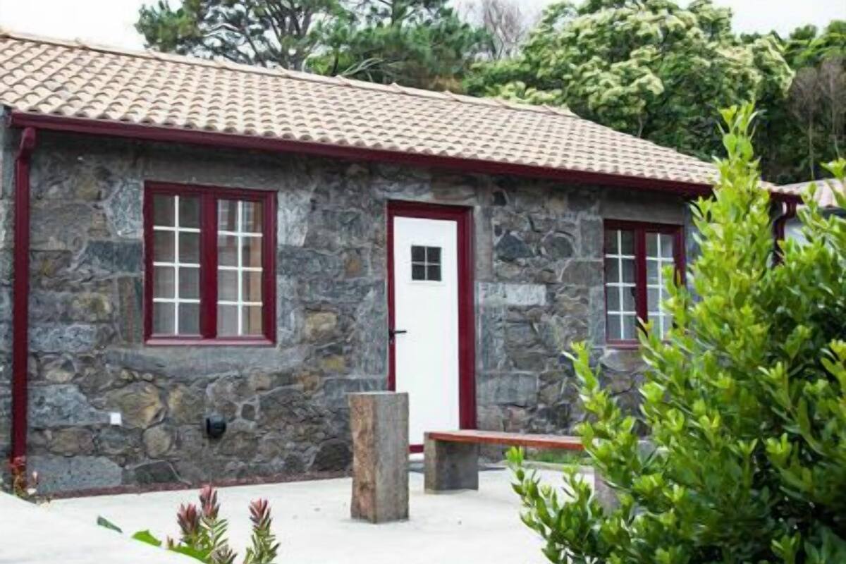 Un edificio de piedra con techo de tejas rojas, una puerta blanca y dos ventanas con marcos rojos.