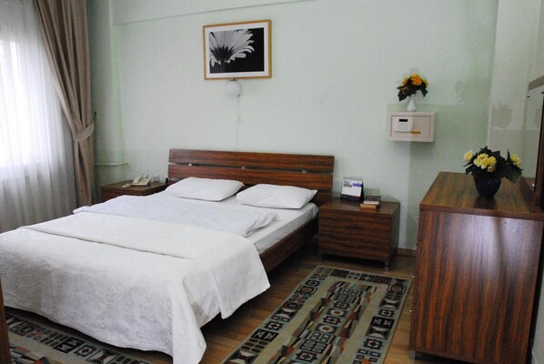 Une chambre d’hôtel comprenant un lit, des tables de chevet, une petite table, un thermostat fixé au mur, un tableau encadré et un vase avec des fleurs.