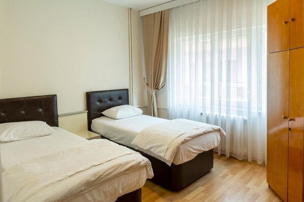 A hotel room with two beds, a wardrobe, and a window with sheer curtains.