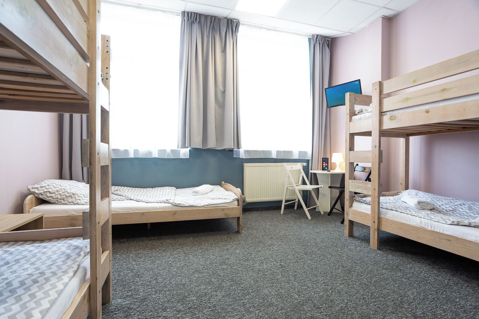 Ein Zimmer mit Etagenbetten, einem Schreibtisch, einem Stuhl, einem Computer und einem fenster mit Vorhängen.