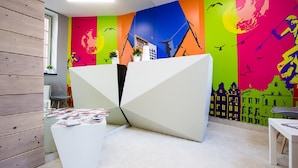 A modern reception area with a colorful mural, a white reception desk, and a seating area with magazines. - Moon Hostel Gdańsk (Gdansk)