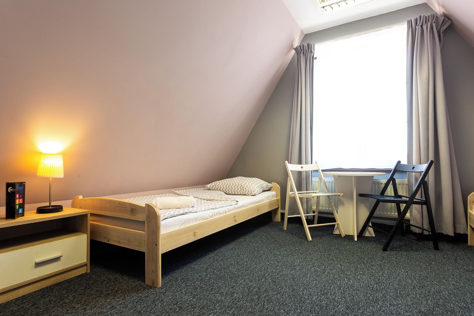 Una habitación pequeña con una cama individual, un escritorio, una silla, una lámpara y un radiador.
