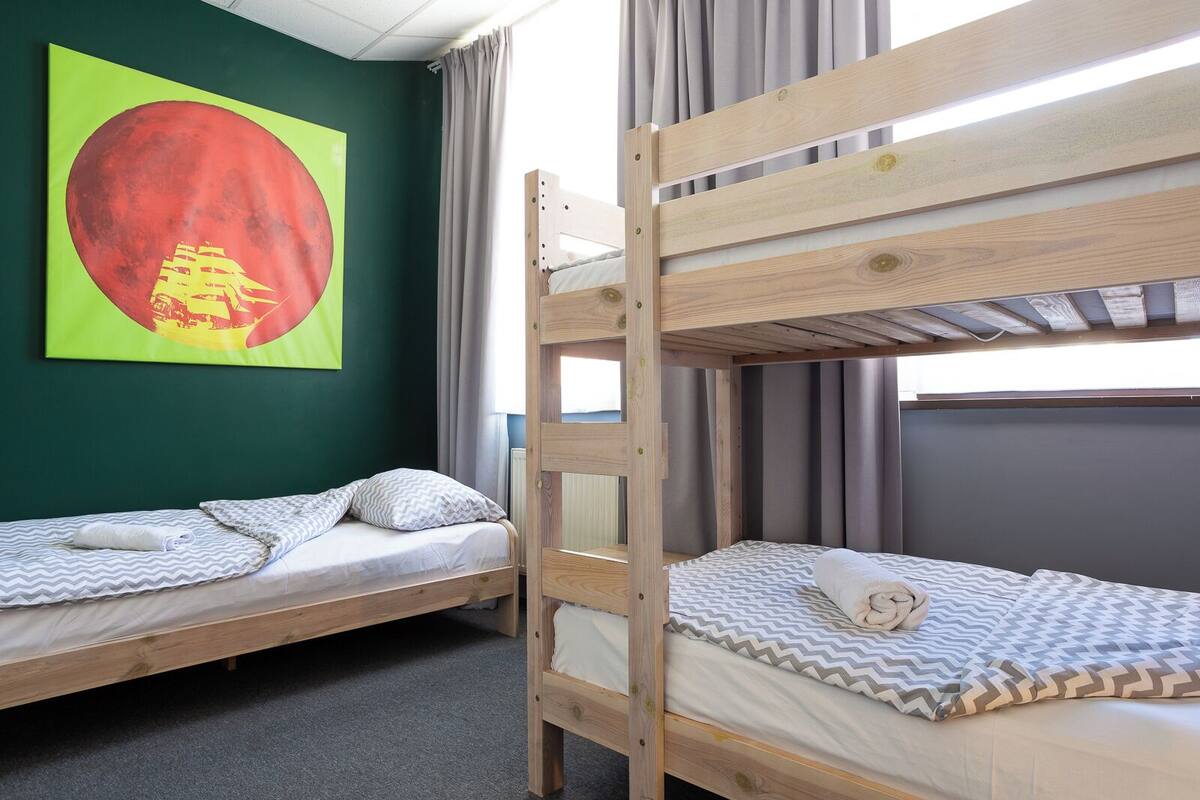 Una habitación con dos literas, una pared verde y un cuadro grande de un círculo rojo.