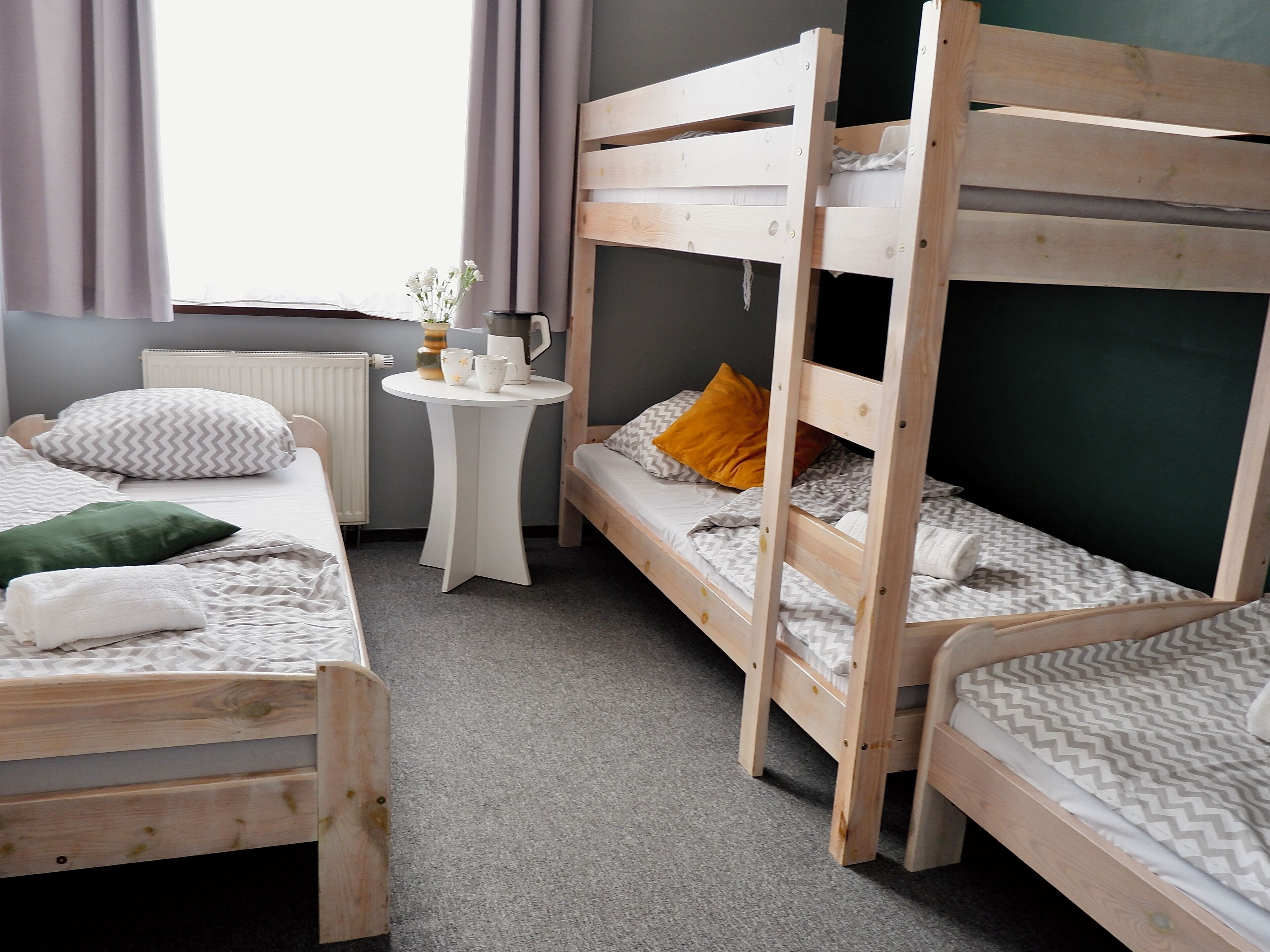 A room with bunk beds, a small round table with a vase and cups, and a radiator.