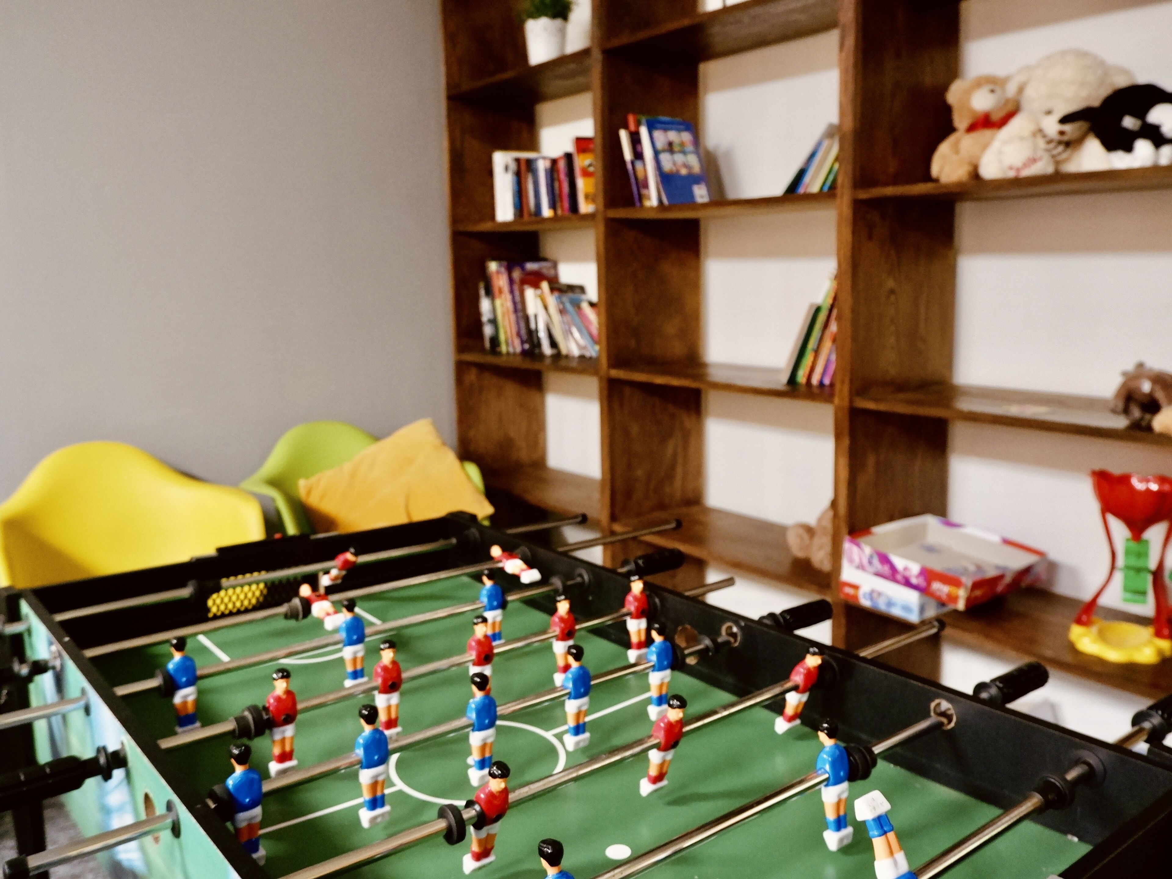 A room with a foosball table, a bookshelf, and a yellow chair.