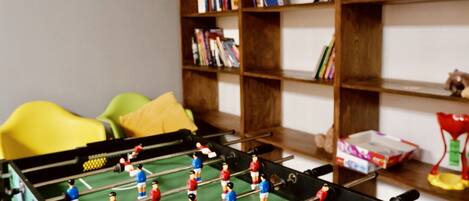 A room with a foosball table, a bookshelf, and a yellow chair.