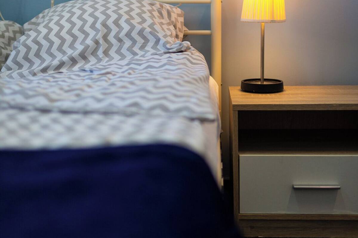 Un dormitorio con una cama, una mesita de noche con lámpara y un velador.