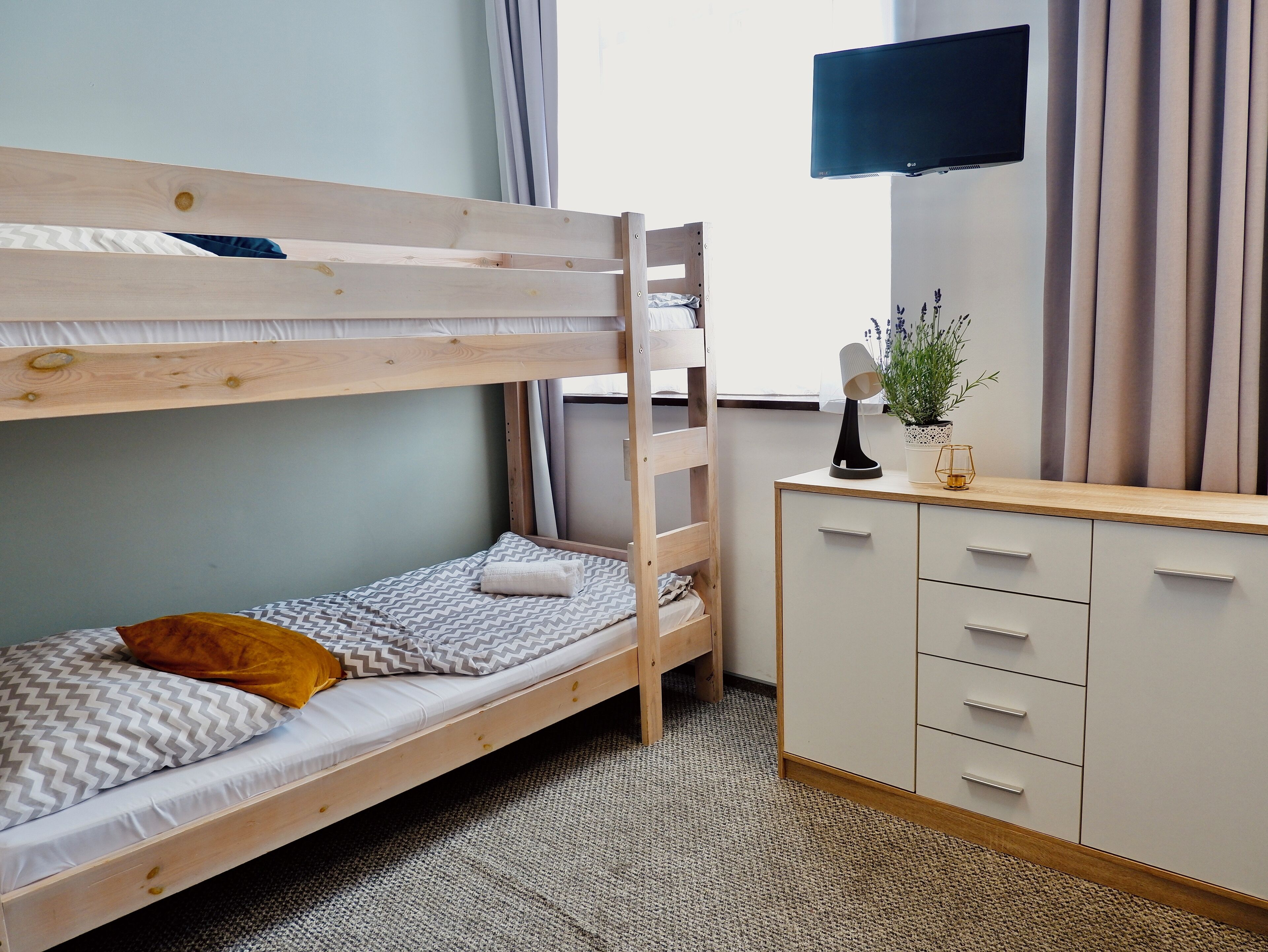 A bunk bed with a desk and drawers, a television on the wall, and a window with curtains.