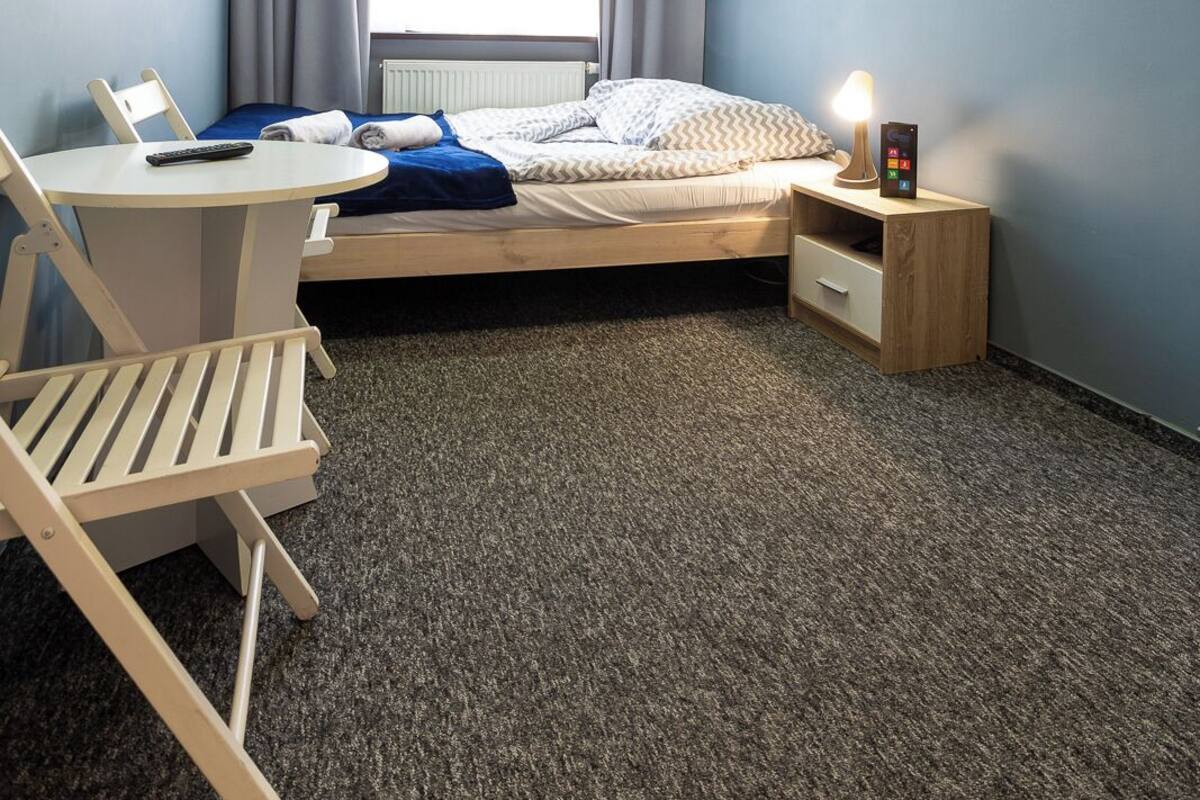 Un dormitorio con cama, escritorio, silla, mesita de noche y lámpara de pared.