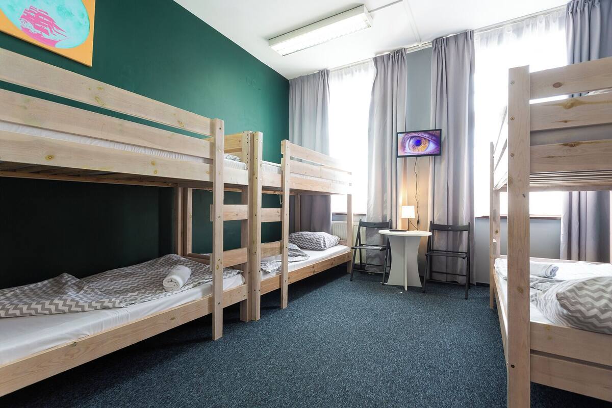 Un dormitorio con literas, una pequeña mesa con sillas, un televisor y una ventana con cortinas.