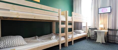 A room with bunk beds, a desk, a chair, a television, and a window with curtains.