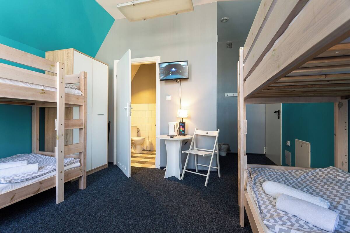 Una habitación pequeña con literas, un escritorio con lámpara y un televisor.