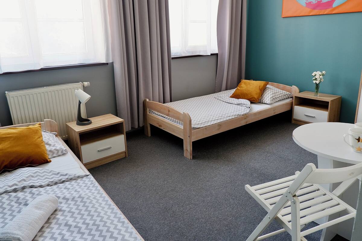 Un dormitorio pequeño y ordenado con una cama individual, una mesita de noche, una silla, una pequeña mesa y un radiador.