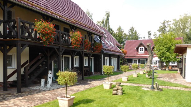 Il s'agit d'un bâtiment traditionnel doté d'une façade en bois sombre, d'un toit en tuiles et d'un jardin bien entretenu, agrémenté de plantes en pot et d'une petite fontaine.