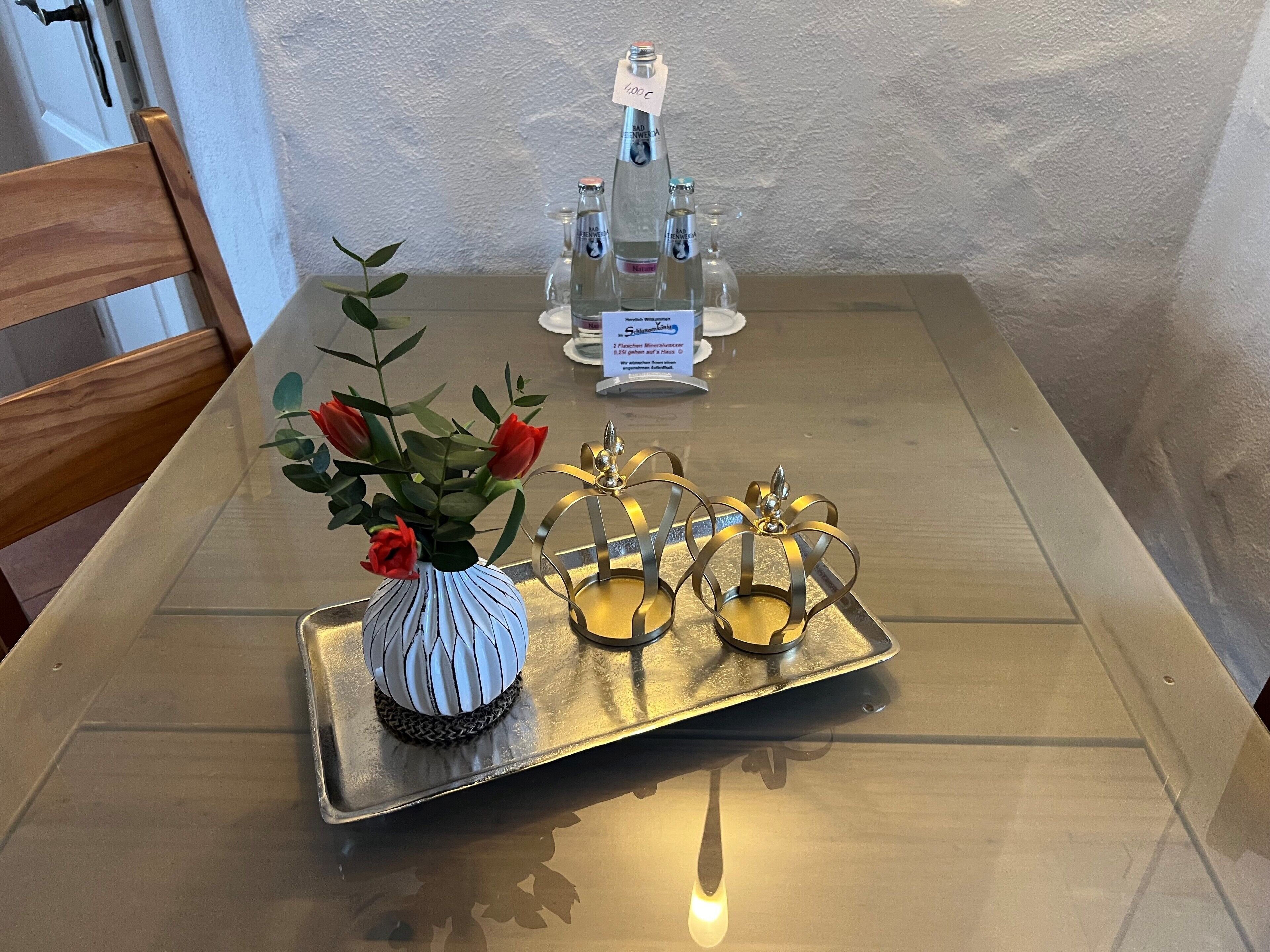 A table with a tray holding a white vase with red flowers, two gold candle holders, and a menu sign.
