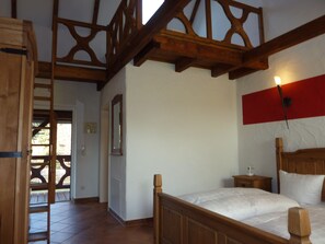 A bedroom with a wooden bed, a nightstand, a wall-mounted mirror, and a red accent wall.