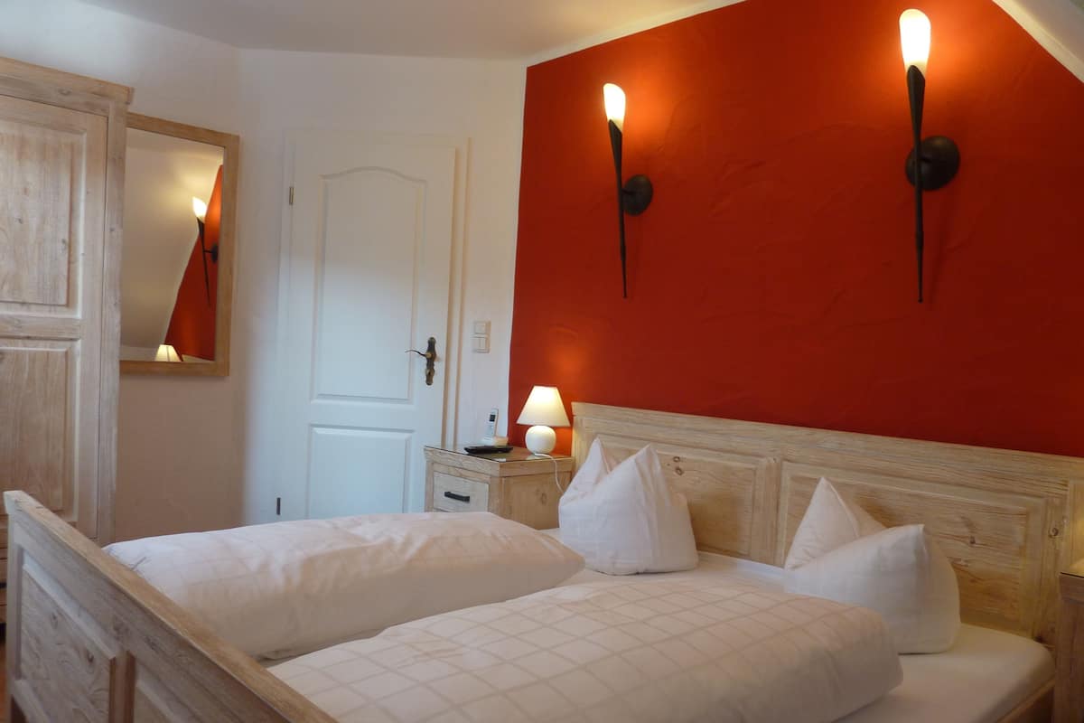 Cama doble con cabecera de madera, mesita de noche con lámpara y un espejo en la pared.