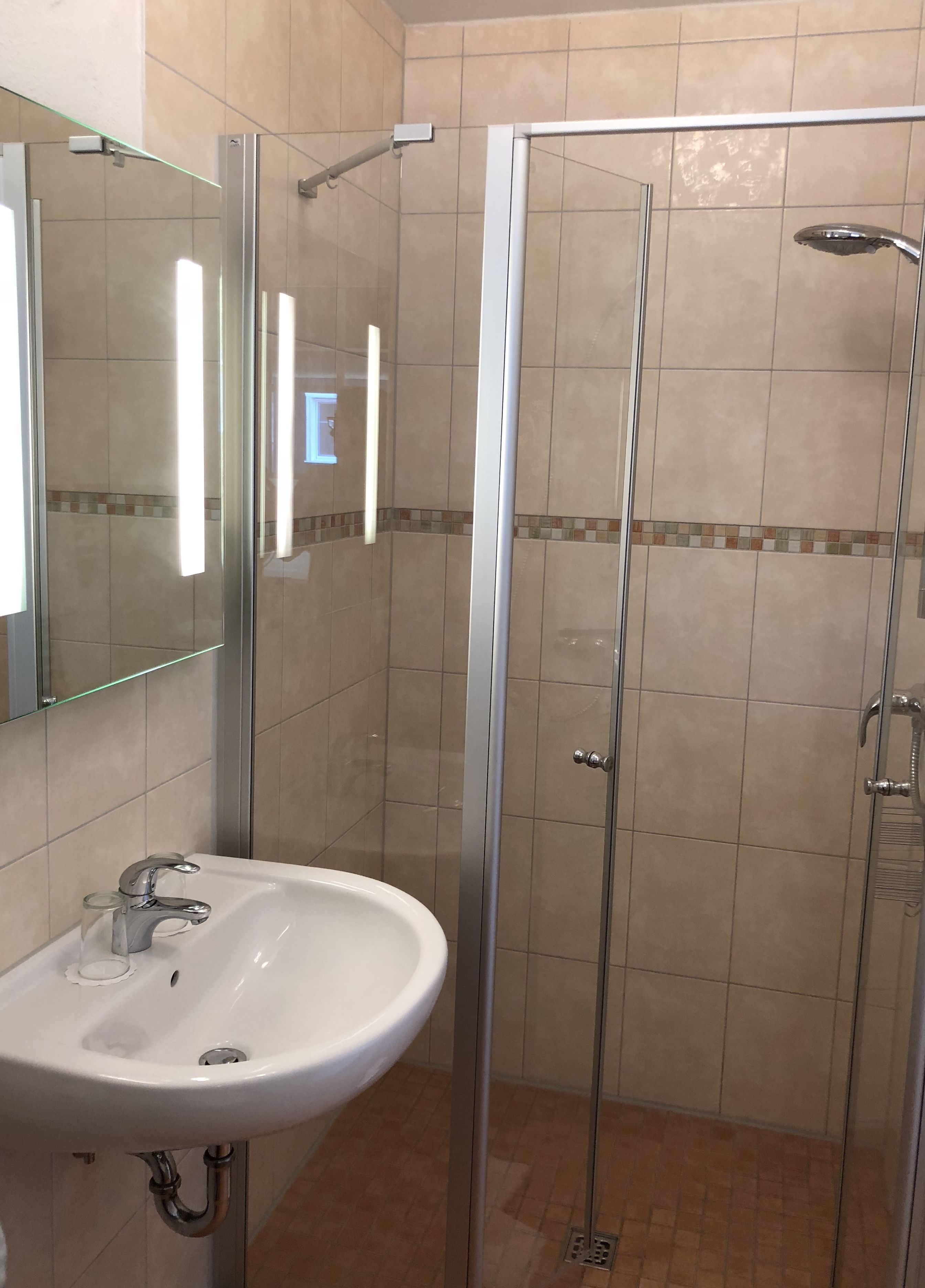 Een badkamer met een douche met glazen wand, een wastafel met spiegel en betegelde wanden.