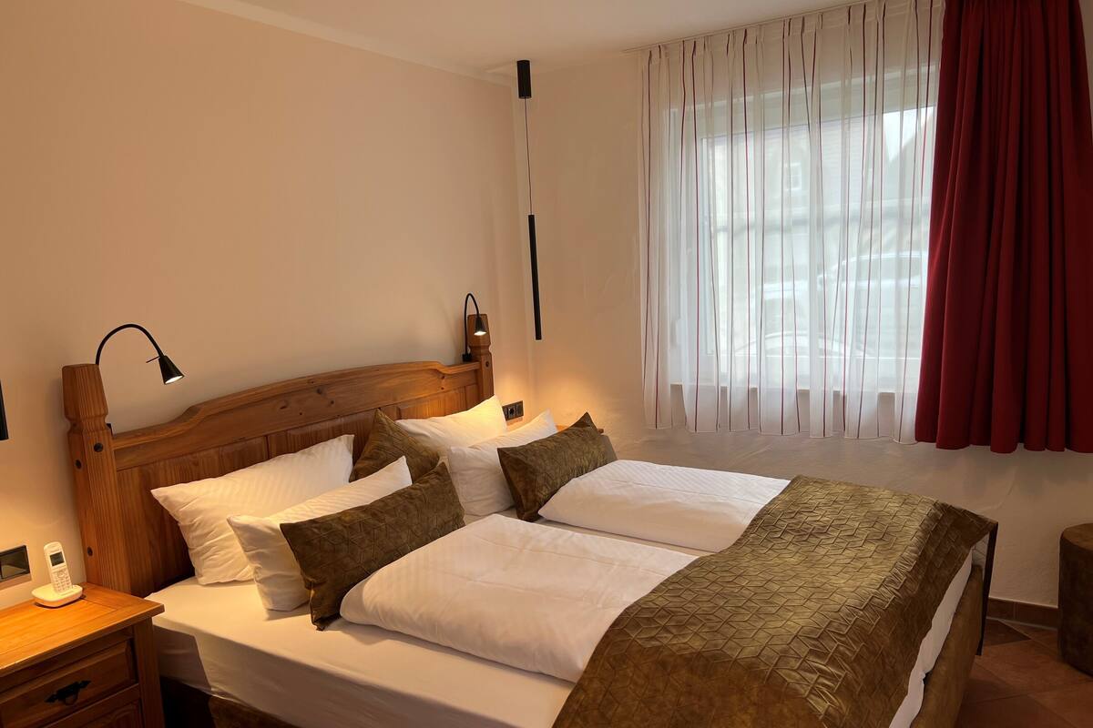 Una cama bien hecha con cabecera de madera, una mesita de noche con lámpara y un teléfono.