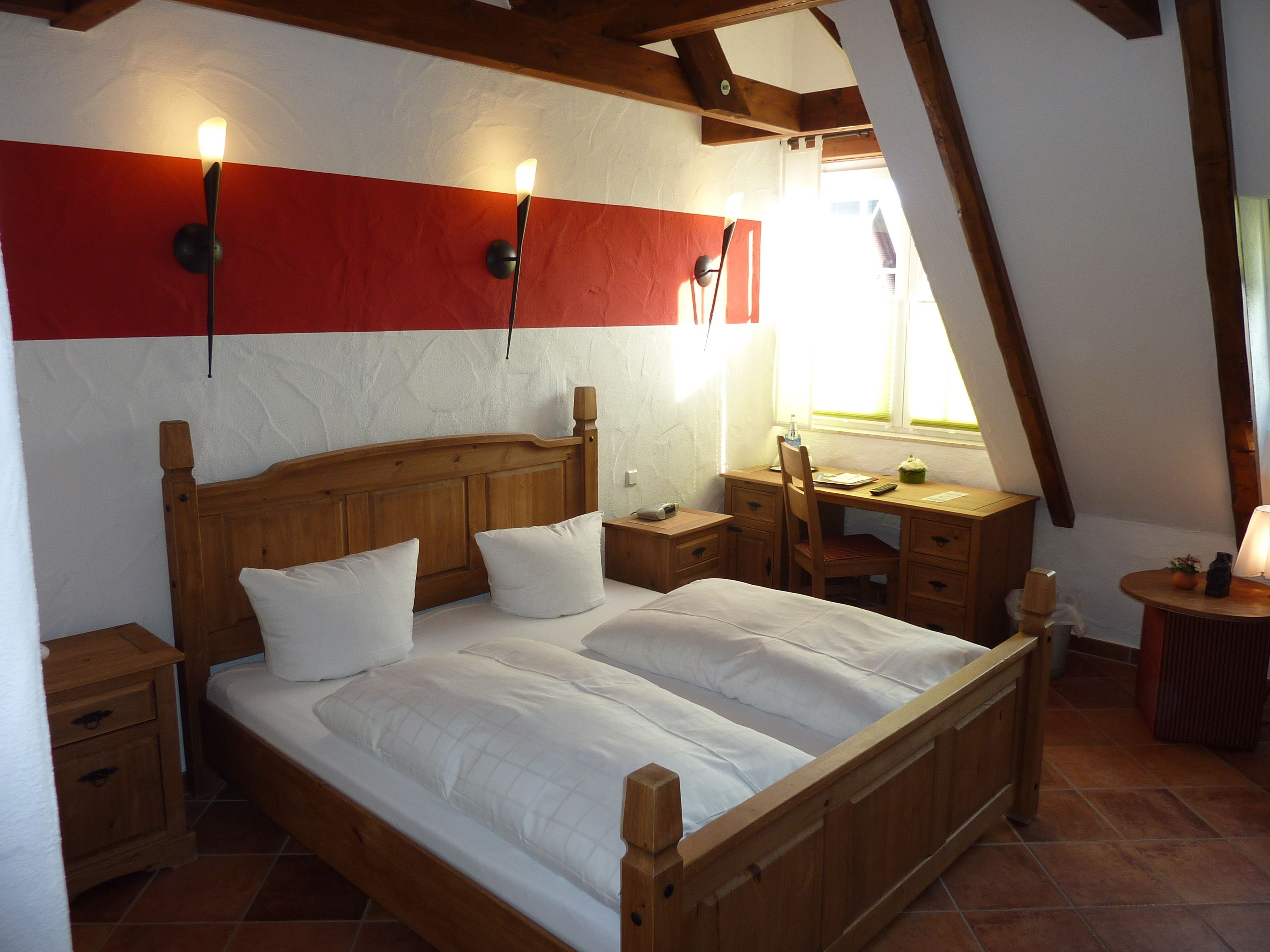 A bedroom with a wooden bed, a desk, and a chair. There are two bedside tables and a window with a view.