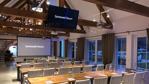 Une salle de conférence au Spreewald Resort, équipée d’un grand écran, de tables en bois et de chaises à motifs.