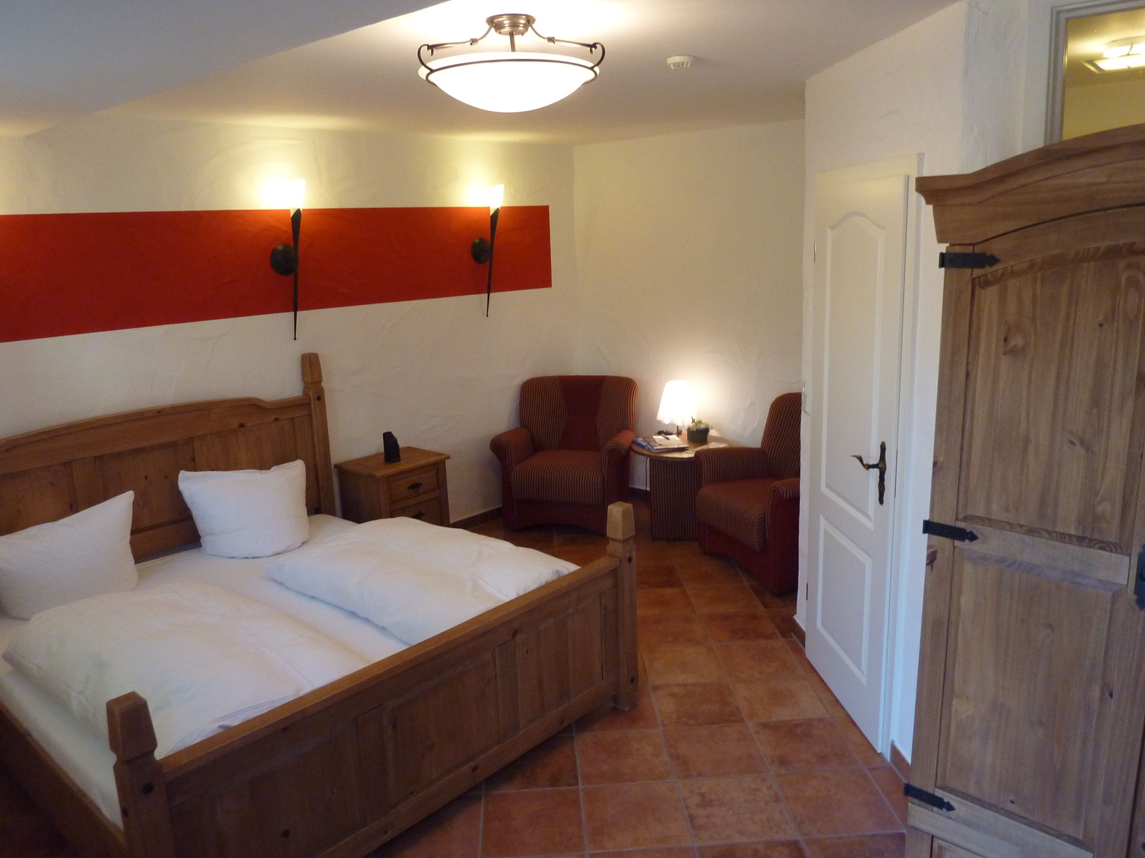 A bedroom with a wooden bed, two nightstands, a chair, a small table with a lamp, and a wardrobe.