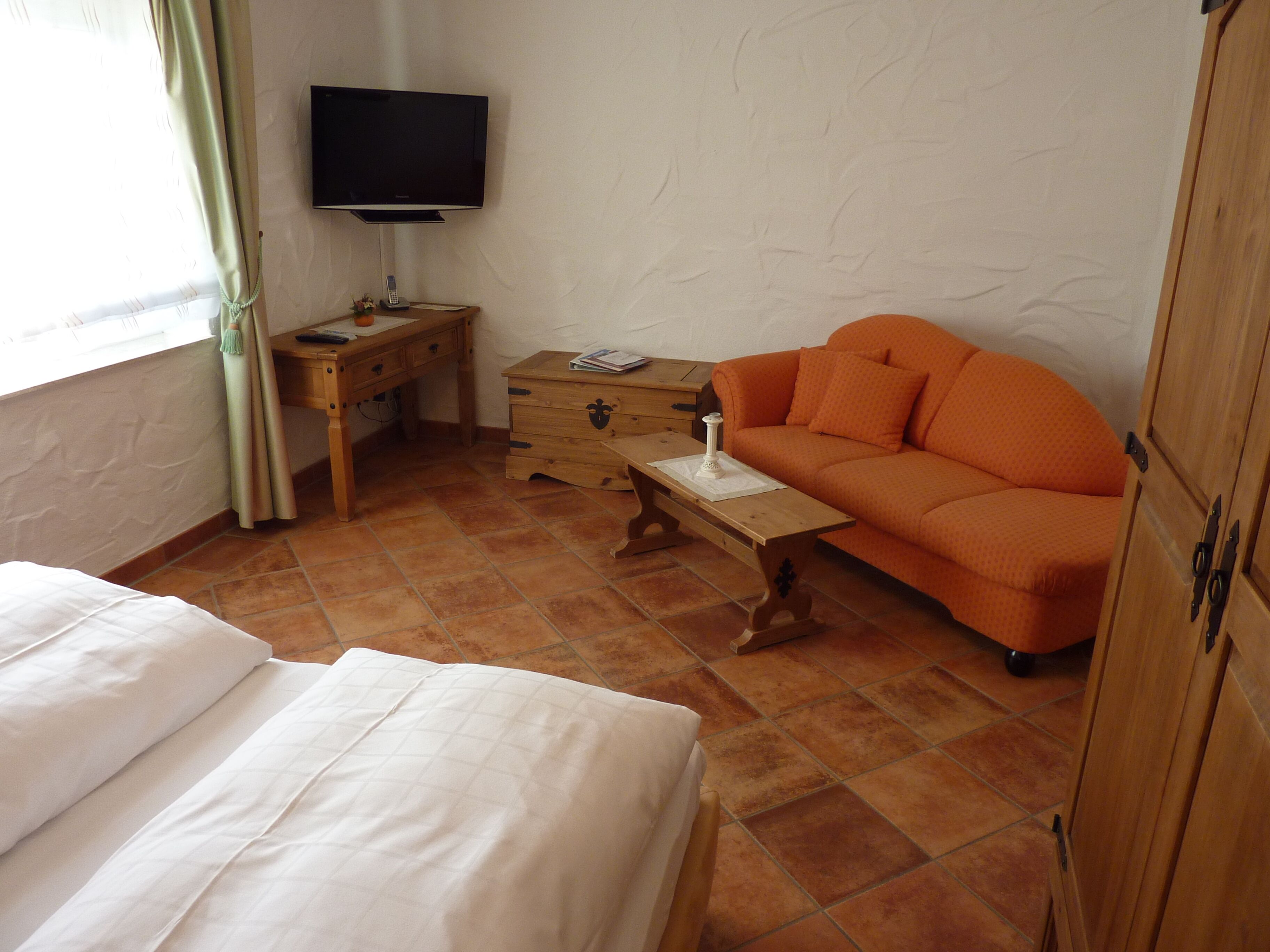 A room with a bed, a wooden nightstand, a television, an orange sofa, and a wooden wardrobe.