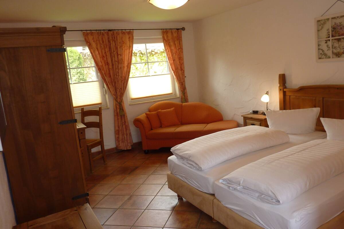 Un dormitorio con cama, cabecero de madera, mesita de noche, lámpara, ventana con cortinas y armario de madera.