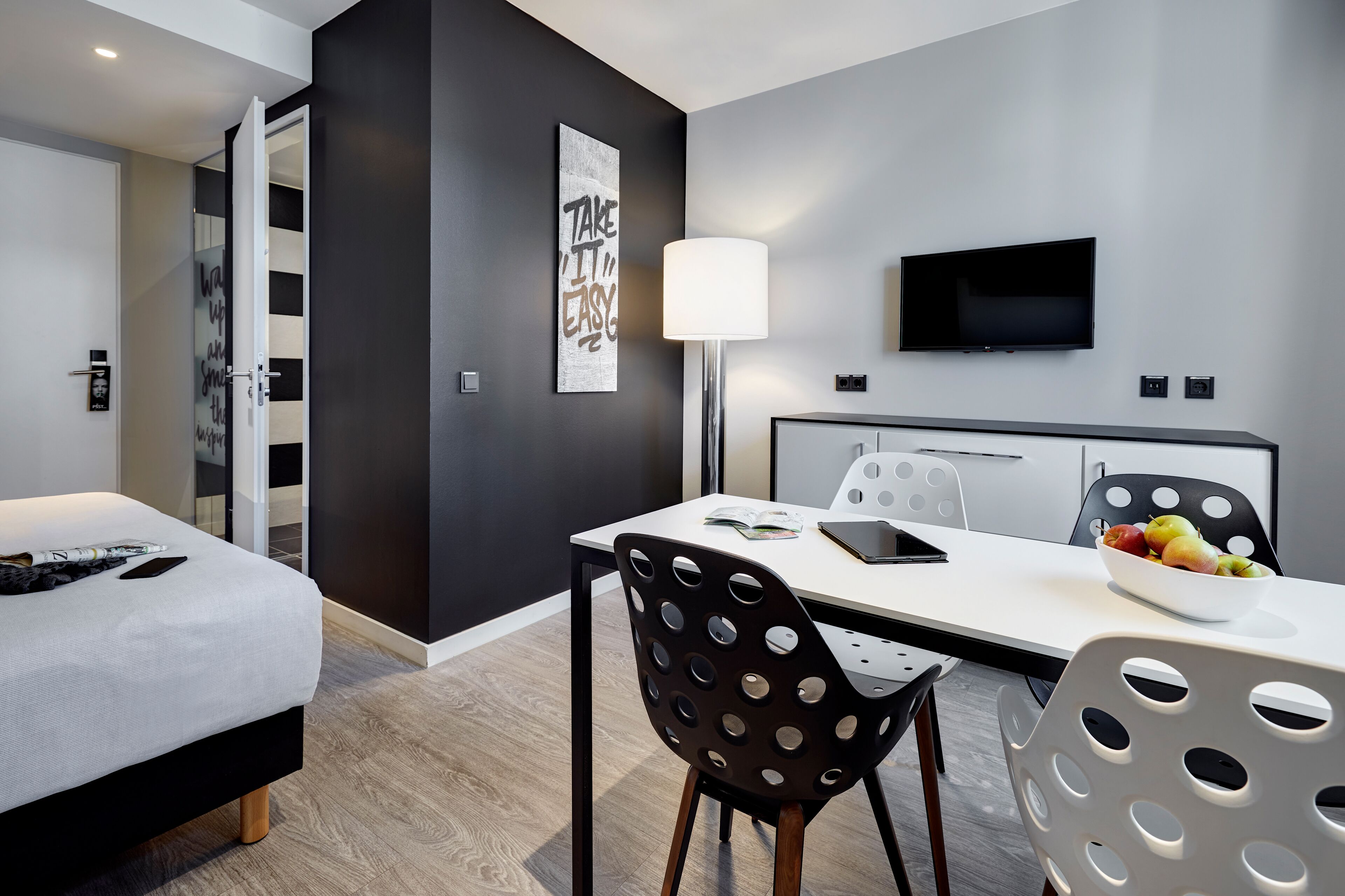 Ein modernes Hotelzimmer mit Bett, Esstisch mit Stühlen, Fernseher und einem motivierenden Wandbild.