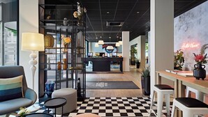 Un vestíbulo de hotel con suelo a cuadros, mostrador de recepción, zonas de estar y un letrero de neón.