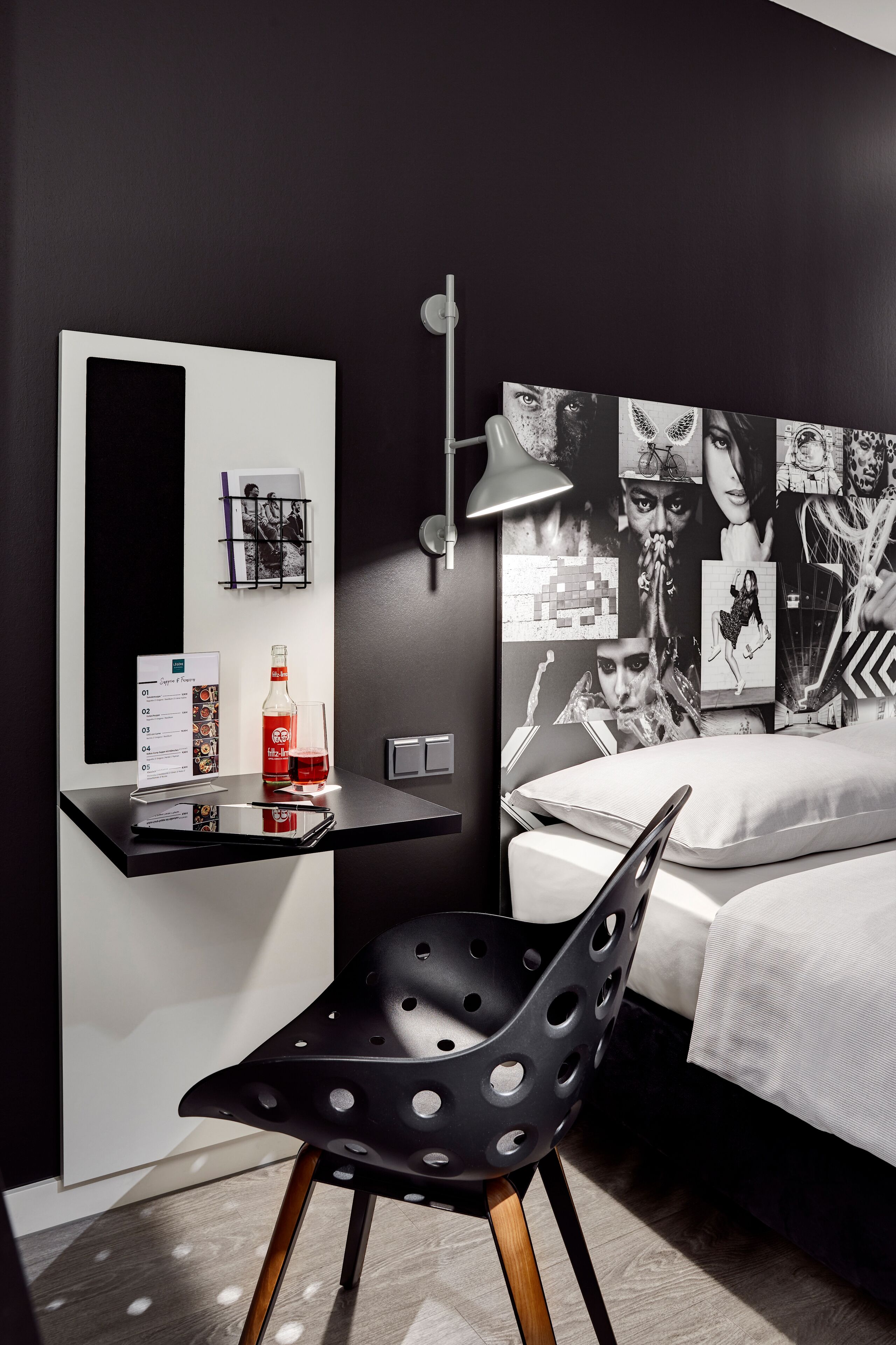 A modern bedroom with a black and white wall art, a desk with a laptop, a chair, and a bed with white bedding.