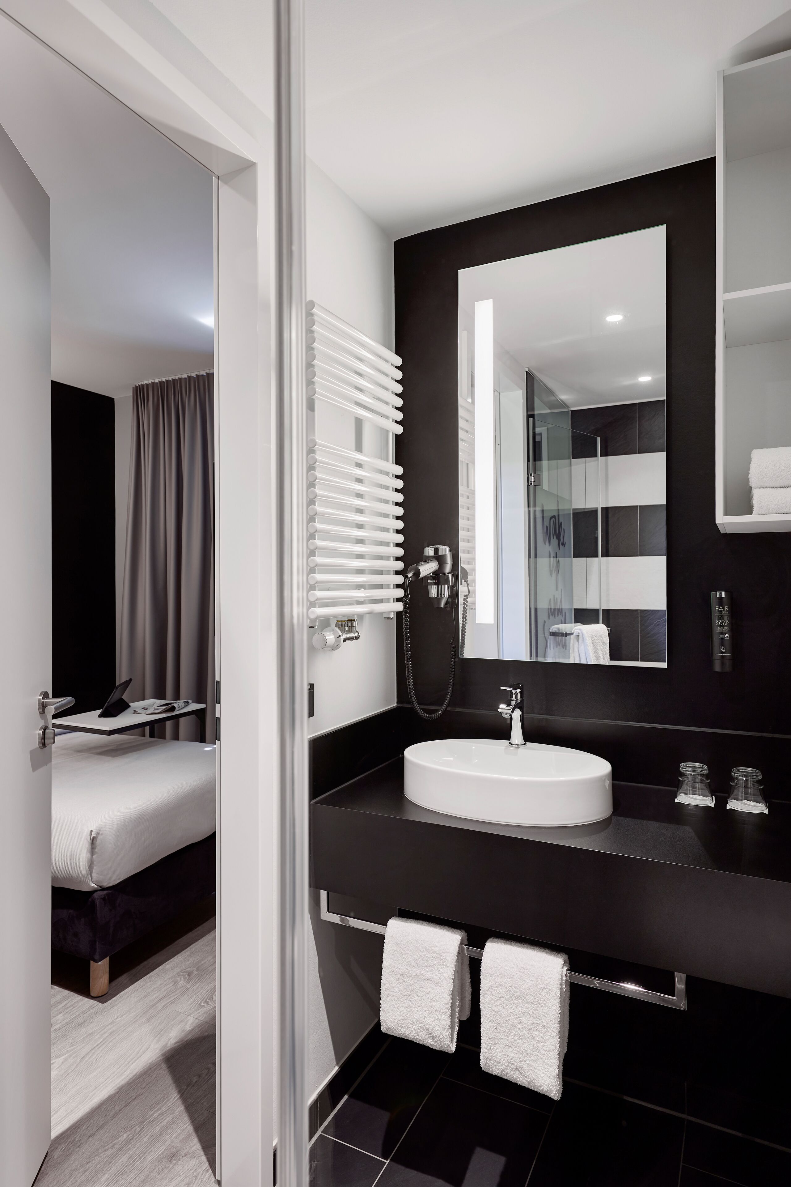 Une salle de bain moderne avec un lavabo blanc, un grand miroir et un porte-serviettes.