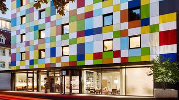 A modern building with a colorful facade, large windows, and a visible storefront with a sign reading "LEGÈRE EXPRESS".