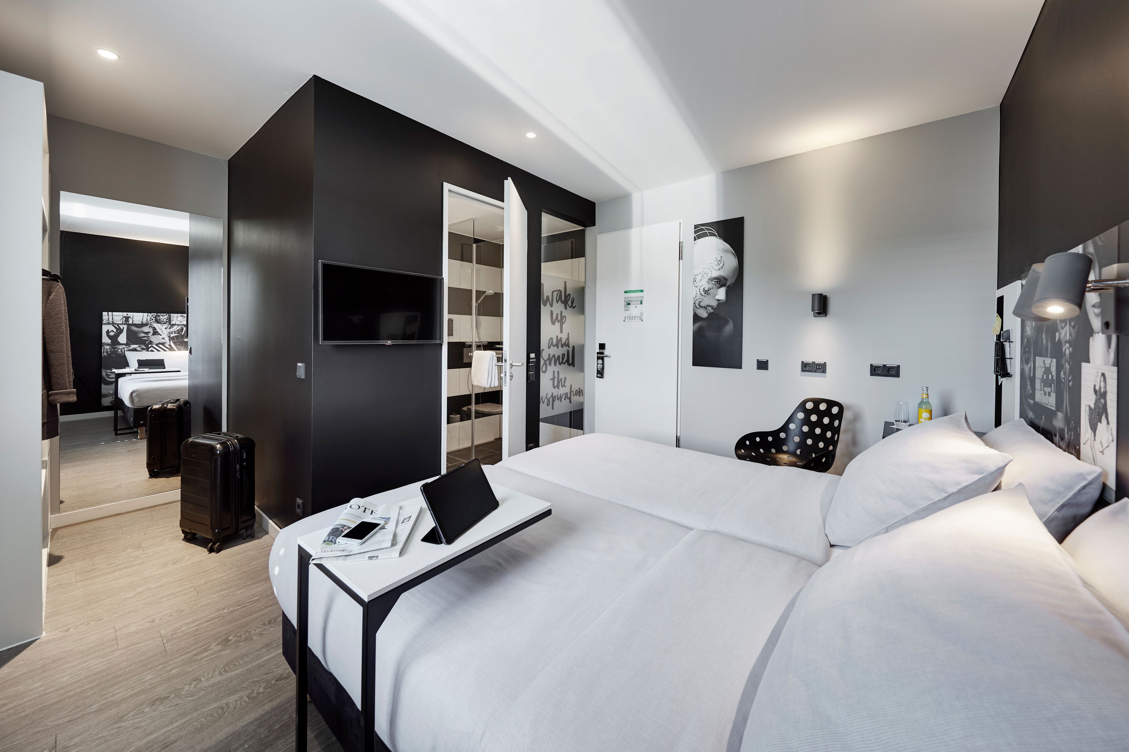 A modern hotel room with a large bed, a desk with a laptop, a chair, and a wardrobe.
