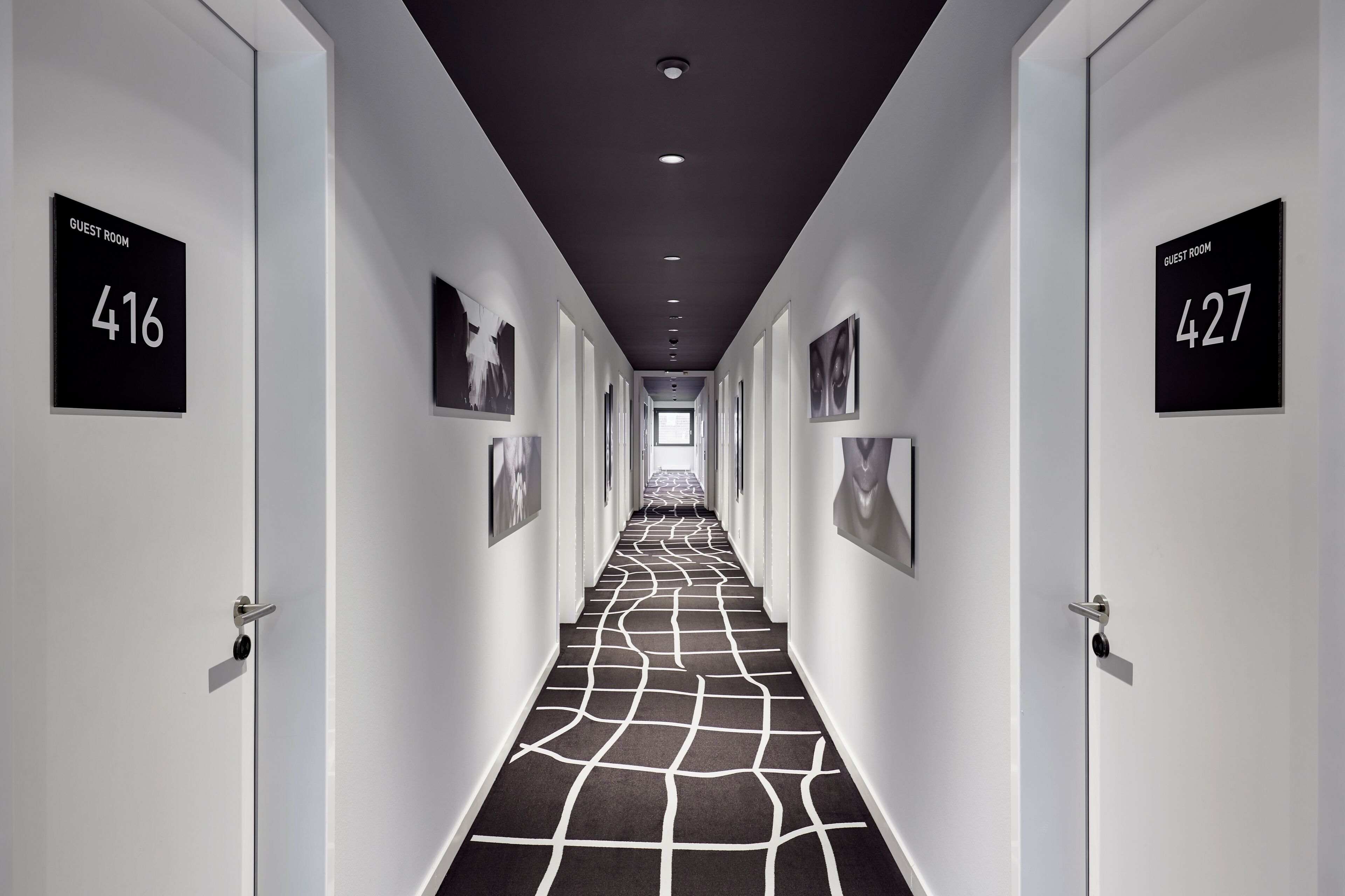 Ein Hotelkorridor mit den Zimmernummern 416 und 427, einem gemusterten Teppich und gerahmten Bildern an den Wänden.