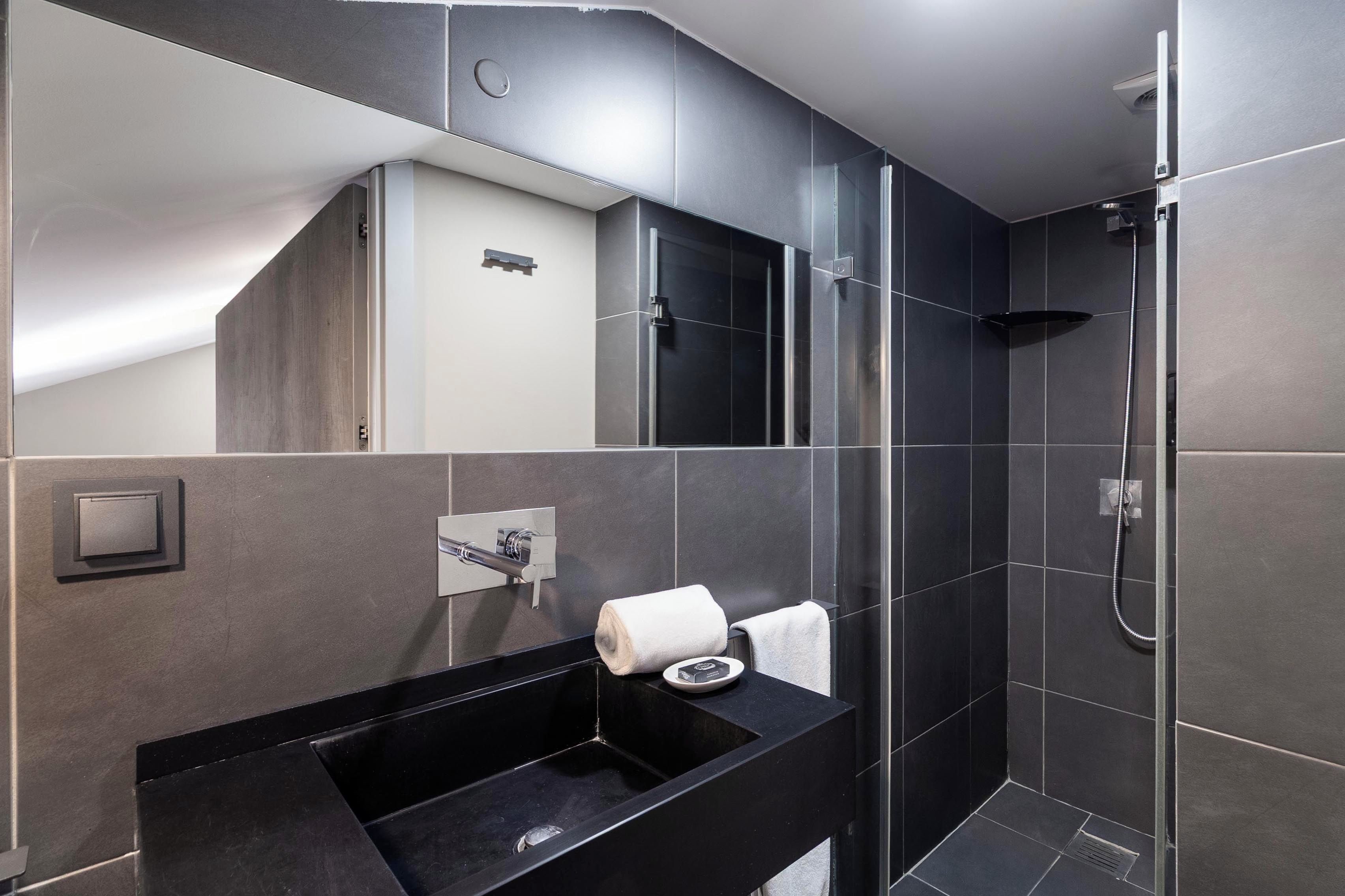 A modern bathroom with a black sink, a mirror, and a shower.