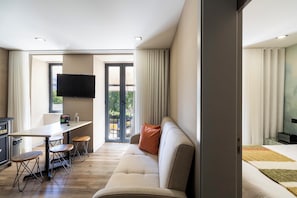 A modern hotel room with a sofa, a dining table with chairs, a flat-screen TV mounted on the wall, and a sliding glass door leading to an outdoor area. - Charm Flats (Lisbon)
