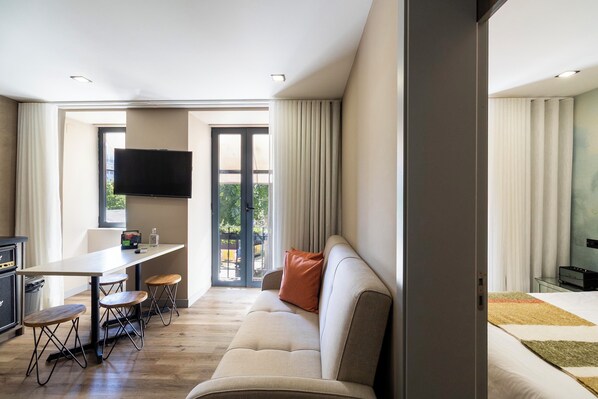 A modern hotel room with a sofa, a dining table with chairs, a flat-screen TV mounted on the wall, and a sliding glass door leading to an outdoor area. - Charm Flats (Lisbon)