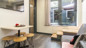 A compact living space with a dining table, four stools, a sofa, and a window with curtains.