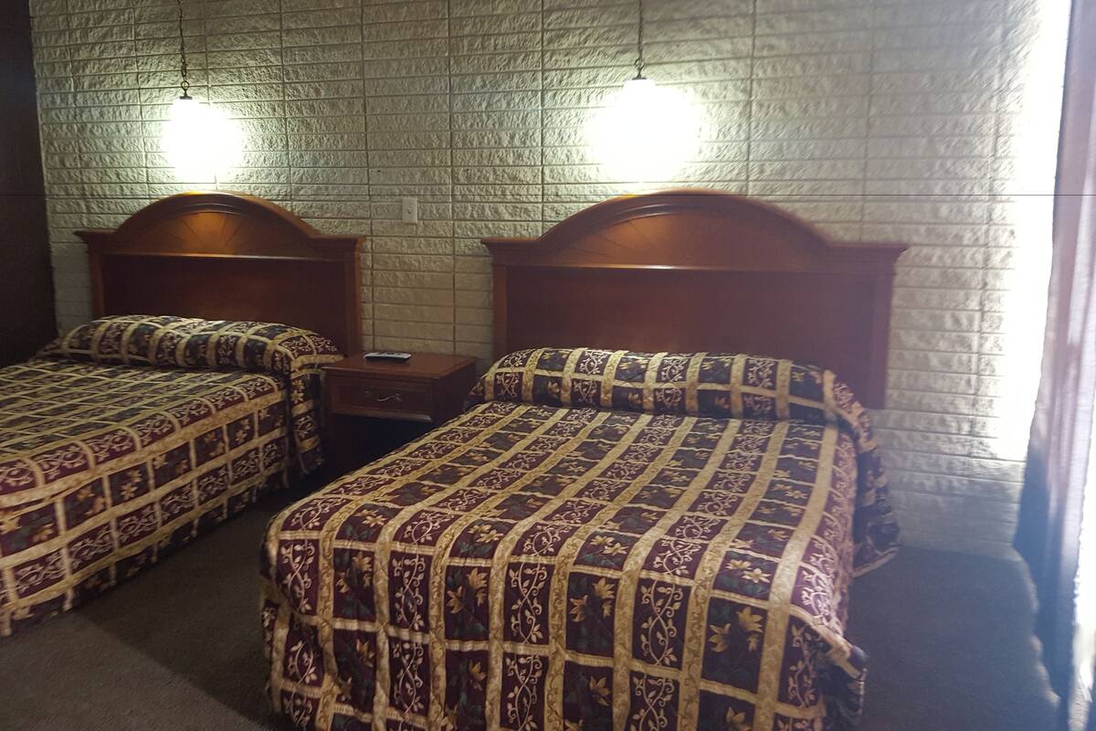 Una stanza con due letti singoli, ognuno con una testiera in legno e biancheria a motivi decorativi. Un comodino è posizionato tra i letti, e le pareti presentano una texture particolare.